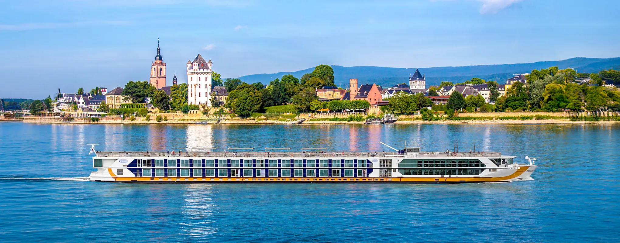 Kreuzfahrtschiff auf einem Fluss vor malerischer Stadt im Sommer.