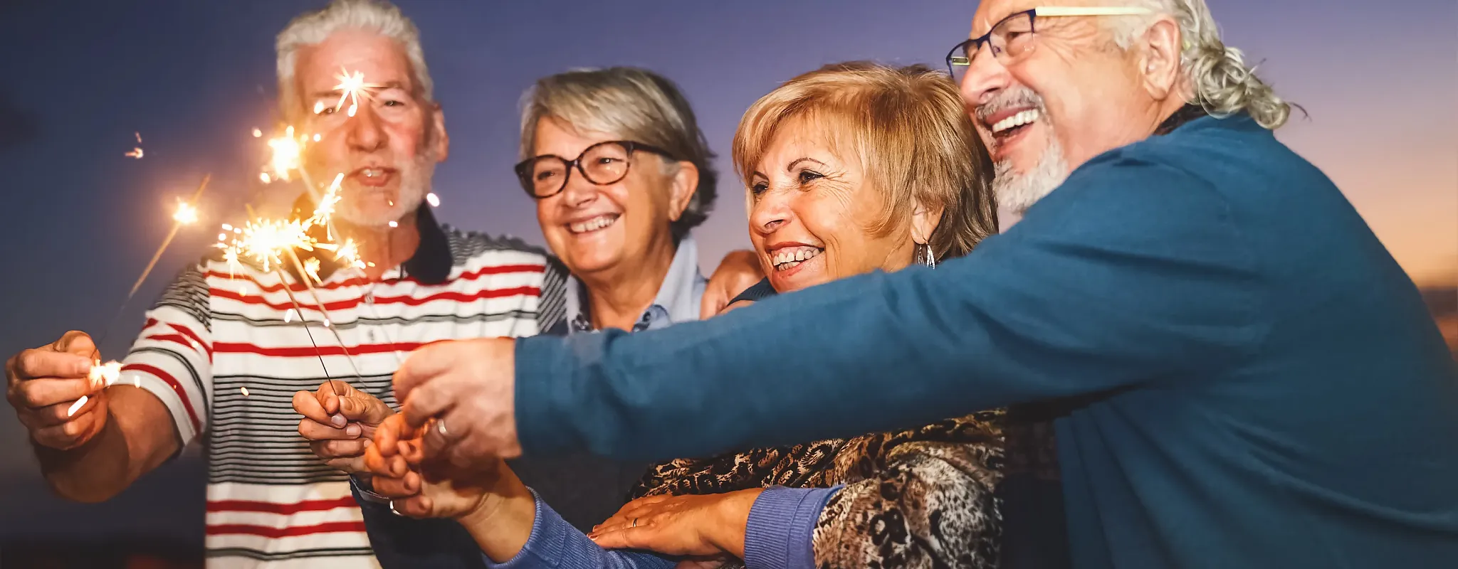 Ältere Menschen feiern mit Wunderkerzen im Freien bei Dämmerung.