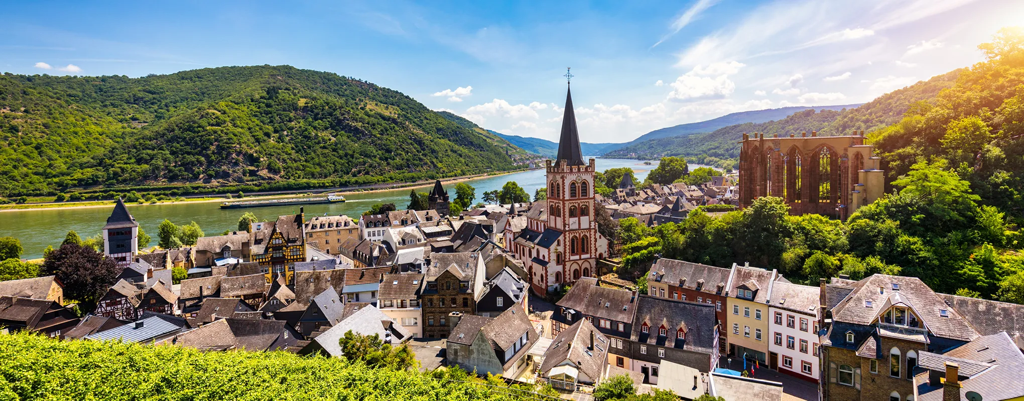 Malerische Rheinlandschaft mit Kirche und Ruine im Sonnenschein.