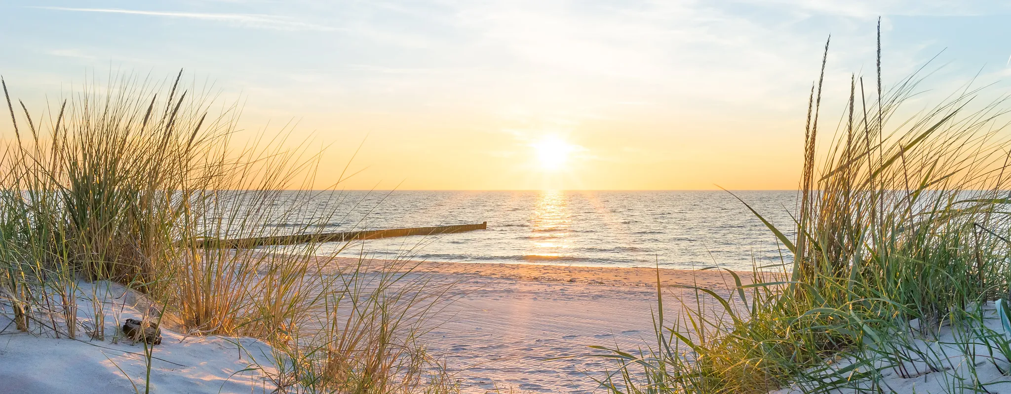 Sonnenuntergang am Strand mit Dünen und ruhigem Meer.