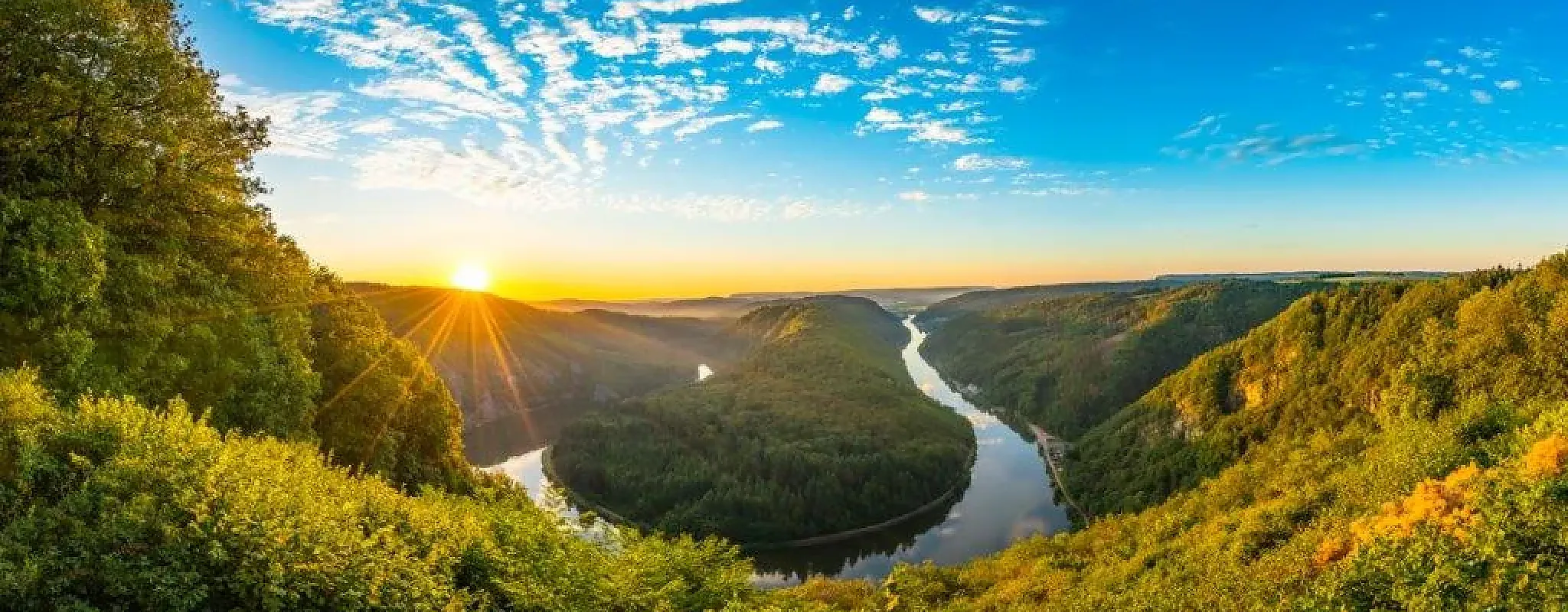 Sonnenaufgang über einem Fluss in malerischer Landschaft.