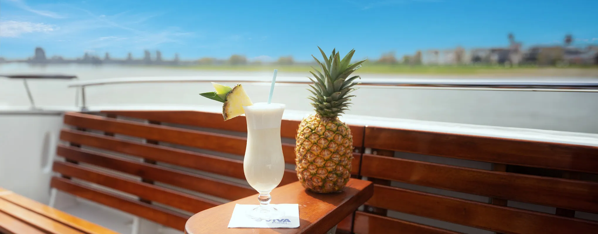 Ananas und Cocktail auf Boot mit Blick auf Fluss und Stadt.