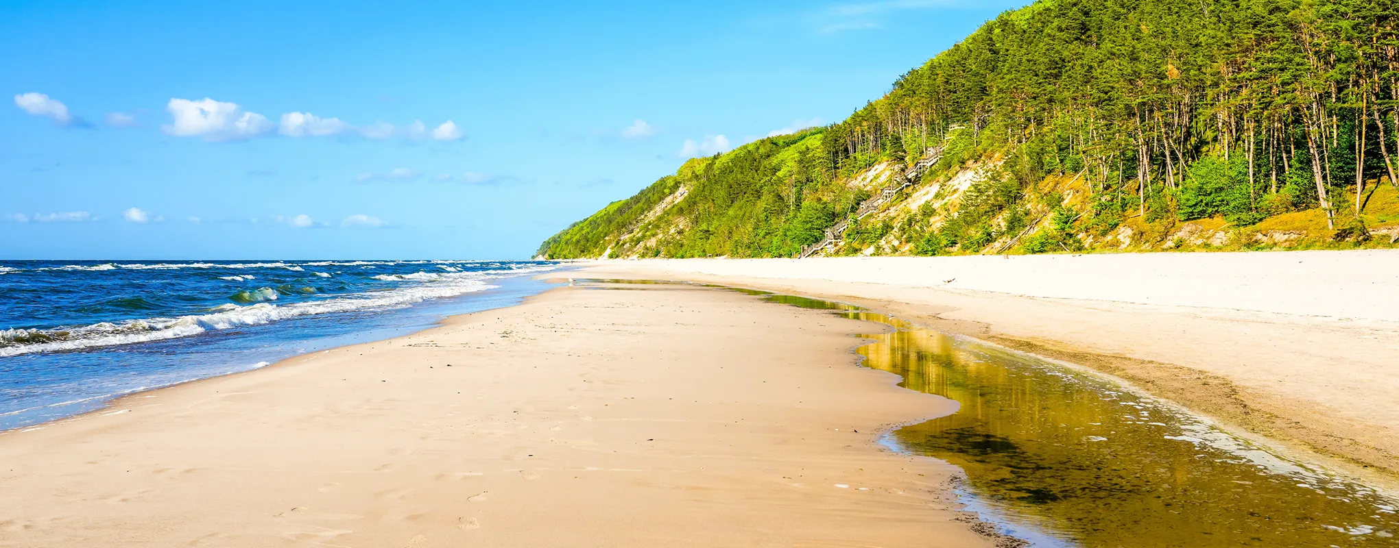 Sonniger Strand an der Polnischen Ostseeküste mit Wellen und Wald.