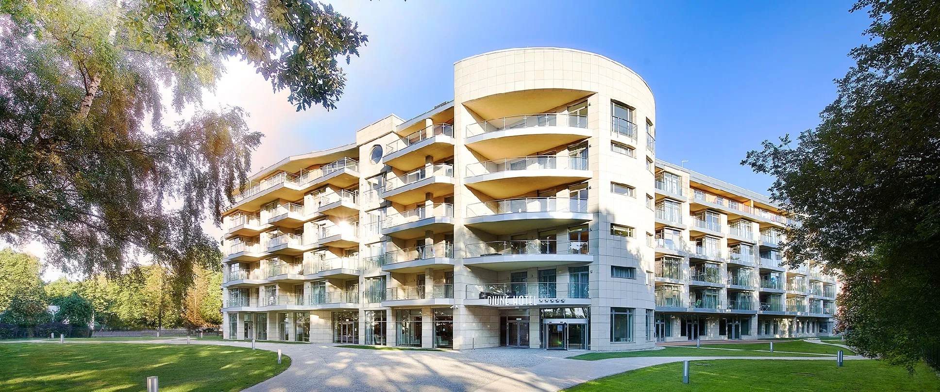Modernes Hotelgebäude in grüner Umgebung, sonnige Atmosphäre.