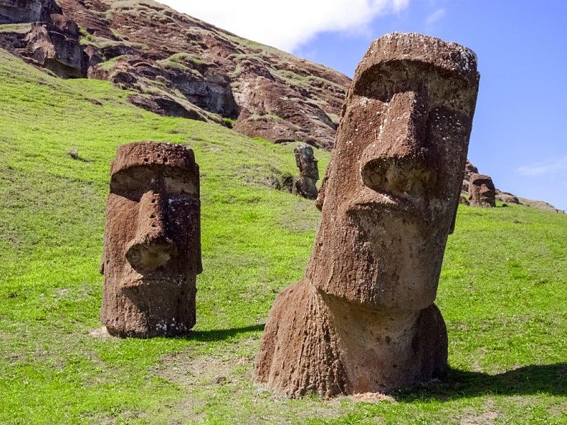 Moai-Statuen auf der Osterinsel vor grüner Hügellandschaft.