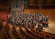 Orchester auf Bühne, Musiker in Konzertsaal, feierliche Stimmung.