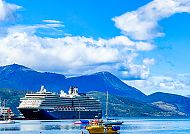 Kreuzfahrtschiff im Hafen von Ushuaia vor Bergkulisse bei Sonnenschein.