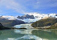 Majestätischer Gletscher mit ruhigem See und Bergen im Hintergrund.