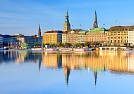 Hamburgs Binnenalster mit spiegelnder Skyline bei klarem Himmel.