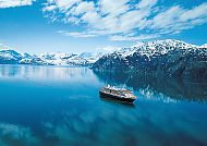 Kreuzfahrtschiff auf ruhigem Wasser vor Alaskas schneebedeckten Bergen.