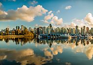 Vancouver Skyline spiegelt sich im ruhigen Wasser unter blauem Himmel.