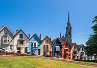 Bunte Häuserreihe in Cobh vor blauem Himmel und Kirche.