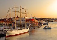 Göteborg, Hafenansicht von Göteborg mit historischem Segelschiff im Sonnenuntergang., Göteborgs Hafen bei Sonnenuntergang mit Segelschiff und Stadtansicht.