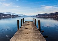 Wörthersee, Steg am Wörthersee im Frühling, umgeben von Bergen und blauem Himmel., Holzsteg am Wörthersee im Frühling, umgeben von Bergen.
