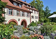 Mainau, Torbogengebäude, Blühende Gartenpracht am Torbogengebäude auf der Insel Mainau., Blühender Garten vor historischem Torbogengebäude auf Mainau.