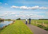 Fahrradfahrer am Fluss, Fahrradfahrer am Flussufer unter blauem Himmel mit Wolken., Fahrradfahrer am Fluss unter blauem Himmel auf der Drei-Flüsse-Tour.