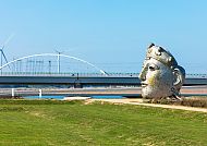 Nijmegen, Skulptur und Brücke in Nijmegen, Holland & Belgien 2026., Skulptur in Nijmegen vor Brücke und Windrädern bei klarem Himmel.