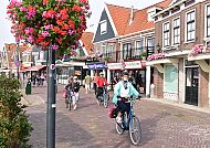 Volendam, Fahrradfahrer in der malerischen Altstadt von Volendam., Radfahrer in Volendam, malerische Straßen und blühende Blumen.