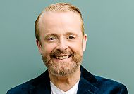 Ross Antony, Ross Antony lächelt freundlich vor grünem Hintergrund., Ross Antony lächelt vor einem schlichten, grünen Hintergrund.