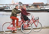 Radfahren auf Norderney, Radfahren am Hafen von Norderney bei frischer Brise und guter Laune., Radfahren am Hafen von Norderney, fröhliches Paar auf Fahrrädern.
