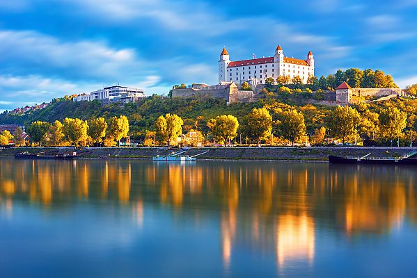 Bratislava, Bratislava: Majestätische Burg über der glitzernden Donau., Bratislava mit der Burg und der Donau bei Sonnenuntergang.