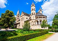 Koblenz, St. Kastor Basilika in Koblenz bei strahlend blauem Himmel., Romanische Kirche in Koblenz, umgeben von grünen Gärten.