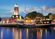 Leuchtturm Kolberg bei Nacht mit beleuchtetem Schiff im Hafen