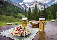 , Bayerische Brotzeit mit Bier vor malerischer Alpenkulisse., Bayerische Brotzeit mit Bergblick in den Alpen bei Lenggries.