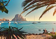 Malerische Küste Ibizas mit Segelbooten und Palmen im Sonnenlicht.