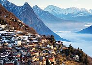 Lugano, Blick auf malerisches Bergdorf mit schneebedeckten Alpen im Hintergrund., Malerische Berglandschaft bei Lugano mit verschneiten Gipfeln.