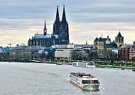 Auf dem Clubschiff den Rhein entdecken, Clubschiff auf dem Rhein mit Kölner Dom im Hintergrund., Flusskreuzfahrt vor dem Kölner Dom bei bewölktem Himmel.