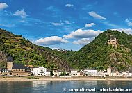 Auf dem Clubschiff den Rhein entdecken, Malerische Rheinlandschaft mit Burgruine und idyllischem Flussufer.