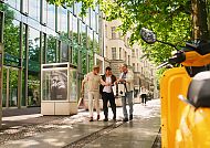 Kudamm Sommer, Sommertag am Ku’damm: Menschen flanieren unter grünen Bäumen., Sommerlicher Spaziergang am Ku’damm unter grünen Bäumen.