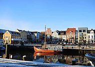 Husum, Husumer Hafen mit historischen Gebäuden und traditionellem Boot., Husumer Hafen mit historischen Gebäuden und traditionellem Segelboot.