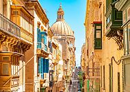 Enge Gasse in La Valletta mit Blick auf eine Kuppel bei Sonnenschein.
