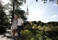 Planten un Bloomen in Hamburg, Paar spaziert im sonnigen Planten un Blomen, Hamburg., Paar spaziert durch Planten un Blomen mit Fernsehturm im Hintergrund.