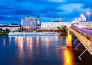 Lichter spiegeln sich im Wasser, Brücke und Gebäude in Linz.