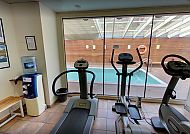Fitnessraum mit Geräten, Blick auf Pool, entspannte Atmosphäre.