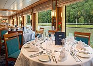 Eleganter Panorama-Salon mit gedeckten Tischen und Flussblick.