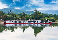 Weiß-rotes Flussschiff vor grüner Landschaft und blauem Himmel