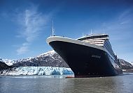 Kreuzfahrtschiff vor Gletscher und Bergen unter klarem Himmel.
