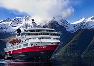 Kreuzfahrtschiff vor schneebedeckten Bergen und ruhigem Wasser.