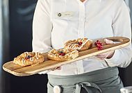 Kellnerin serviert Gebäck mit Beeren auf Holzbrett, gemütliche Stimmung.