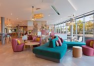 Heller, moderner Lounge-Bereich mit bunten Möbeln und großen Fenstern.