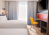 Modernes Hotelzimmer mit zwei Betten, gelbem Stuhl und TV.
