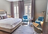 Modernes Hotelzimmer mit Doppelbett, Sesseln und Schreibtisch.