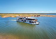 African Dream, Luxus-Schiff auf ruhigem Wasser, Elefanten im Hintergrund., Luxus-Schiff auf Fluss mit grasenden Elefanten im Hintergrund.