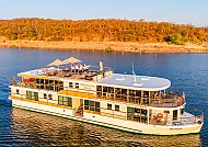 Zimbabwean Dream, Luxuriöses 5-Sterne-Schiff auf einem ruhigen Fluss bei Sonnenuntergang., Luxus-Schiff auf ruhigem Fluss vor herbstlicher Landschaft.