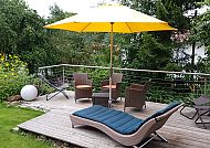 BIO Sportpension, Gemütliche Terrasse mit Liege und gelbem Sonnenschirm im Grünen.