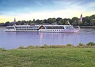 MS Compass Opera vor grüner Landschaft, MS Compass Opera auf ruhigem Fluss vor grüner Landschaft.